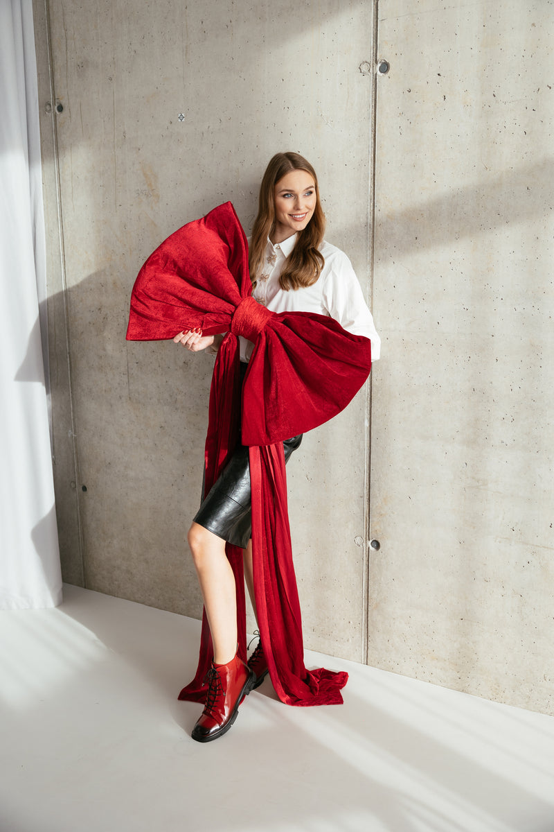 Woman holding a large red bow against a concrete wall